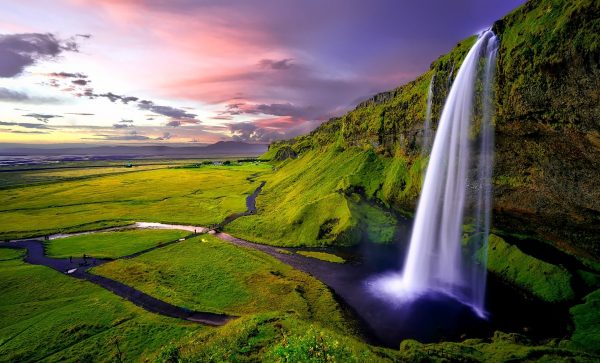 A spectacular waterfall decending from a verdant green cliff.