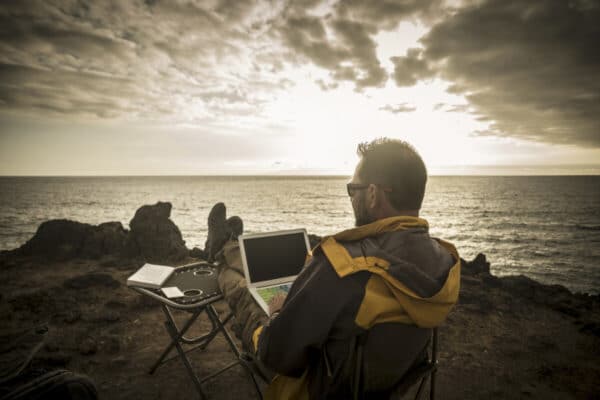 Man working on a laptop with an ocean view. The best part of the employee travel experience.