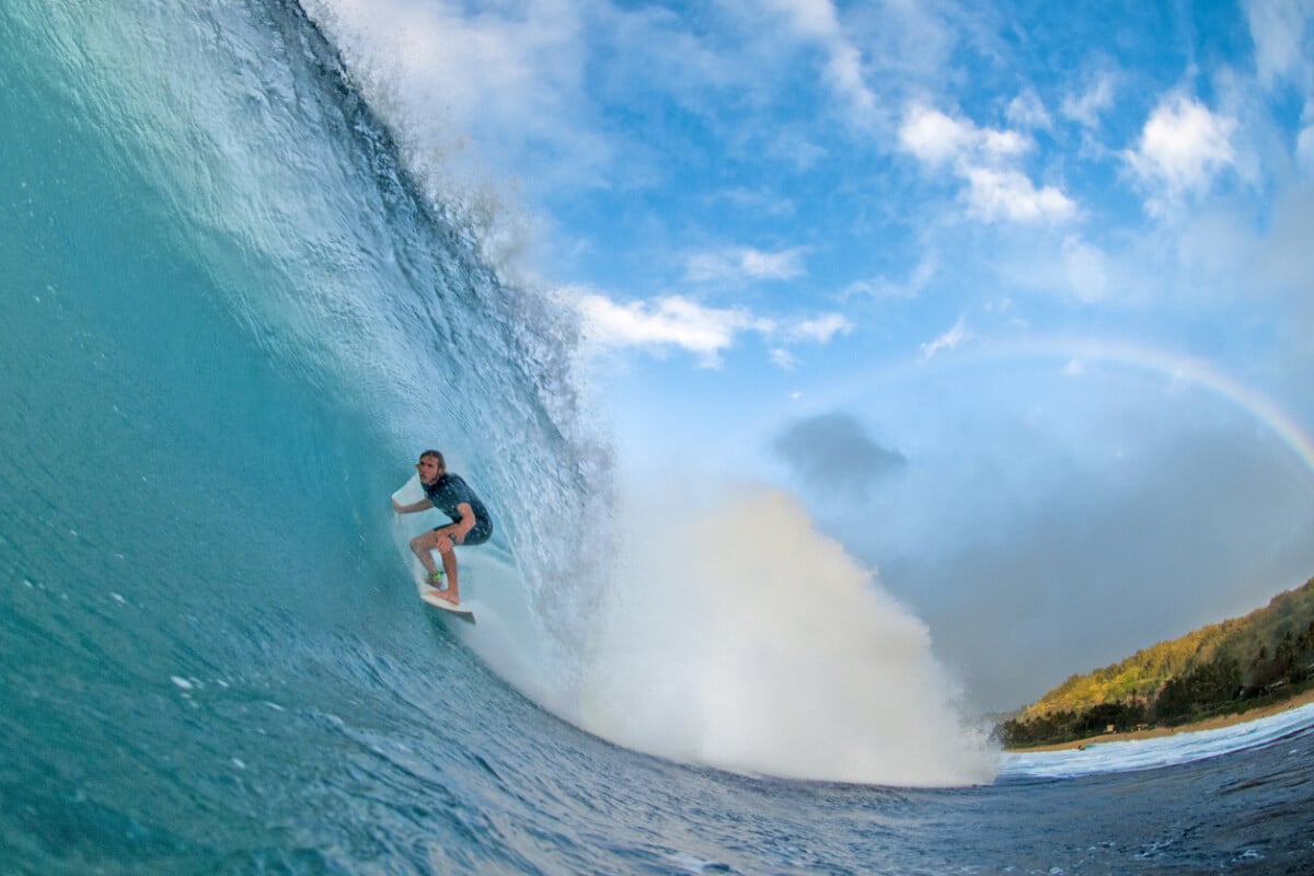 A professional surfer rides a perfect North Shore barrel with a rainbow in the background