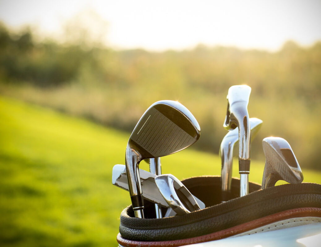 Golf clubs drivers over green field background. Summer sunset. Photo by petrenkod via iStock by Getty Images