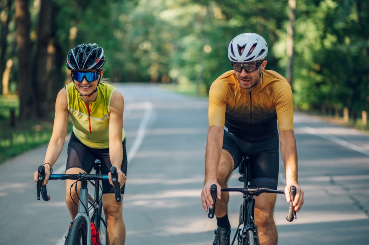 Portrait of a happy couple riding road bicycles outside. Healthy lifestyle and fun concept. Athletic couple riding while wearing sports clothing, protective helmets and sunglasses. Copy space.