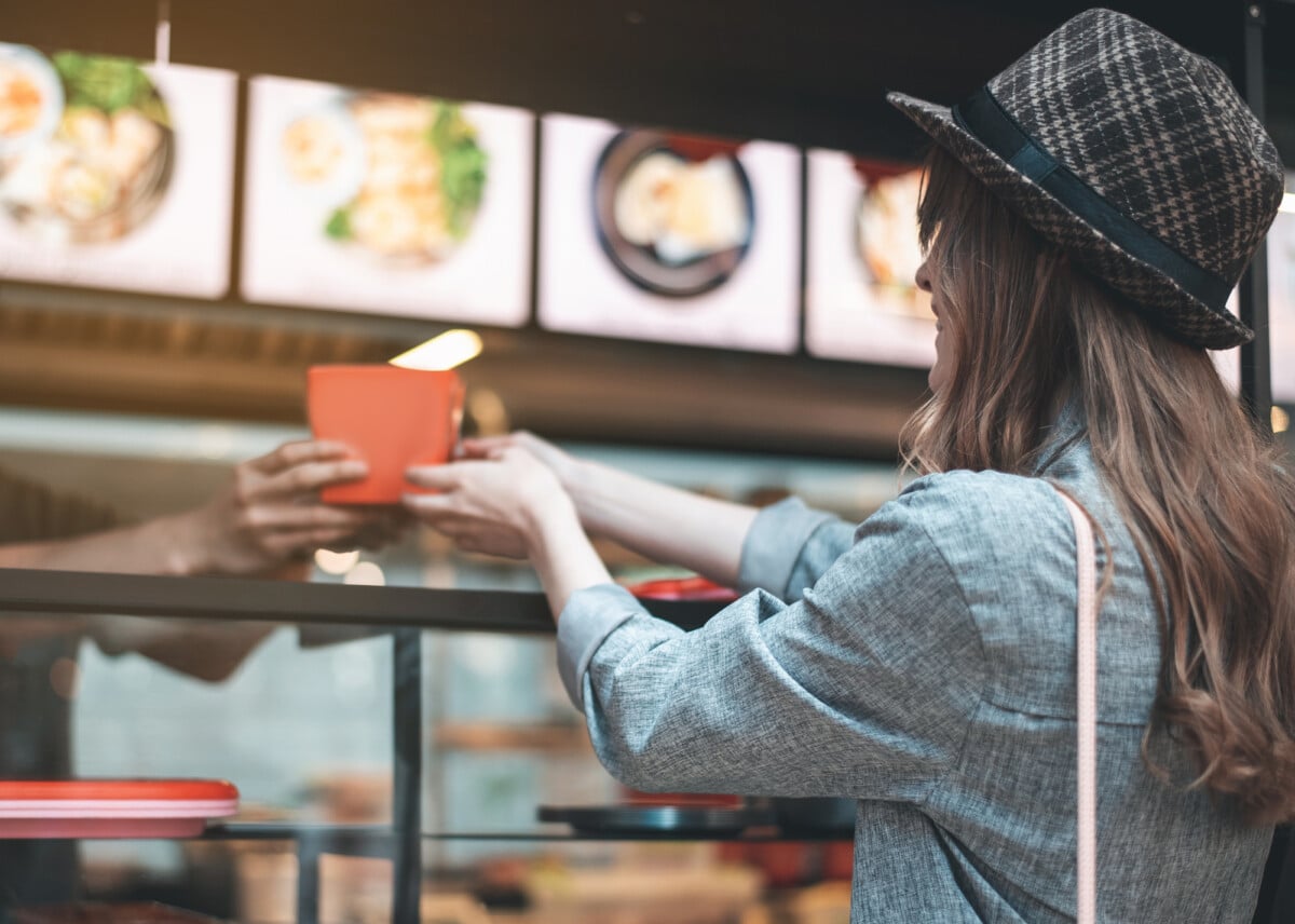 Smiling lady is taking asian meal from waitress. She is standing at counter in trendy hat back