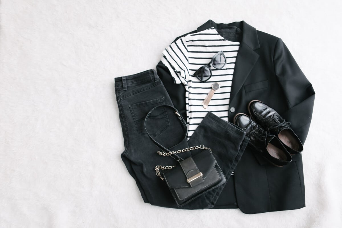 overhead flat lay view woman clothes black and white handbag jeans blazer shoes sunglasses