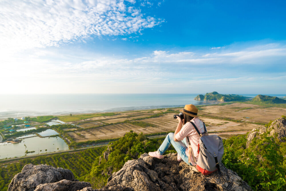 Asian hipster girl sitting on the peak of mountain with camera. Landscape recreation.