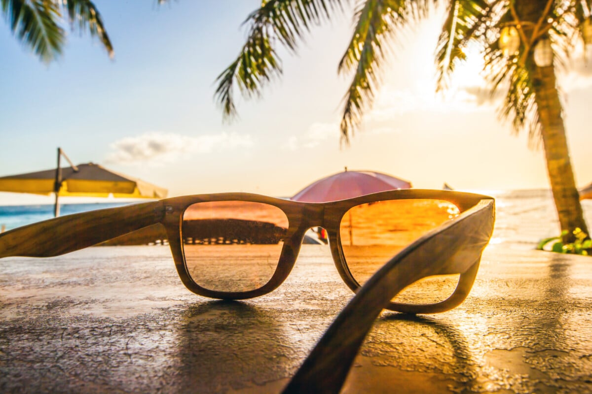 Sunglasses on tropical beach with palms at sunset