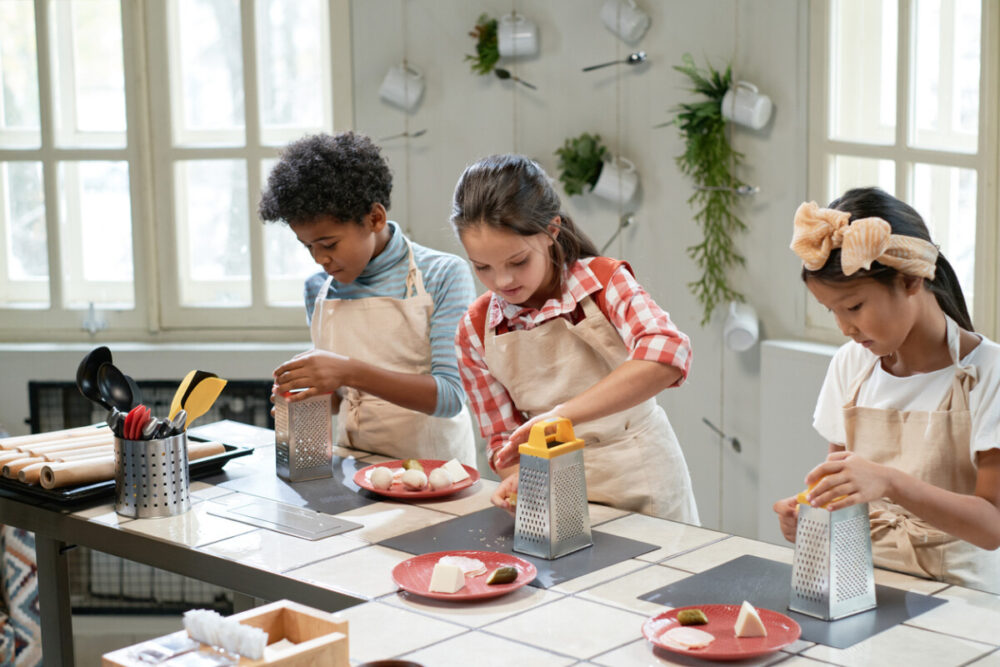 How to Keep Children Engaged During a Vacation 6 Group of children in aprons rubbing cheese on the plates while standing at the table, they cooking pizza during lesson