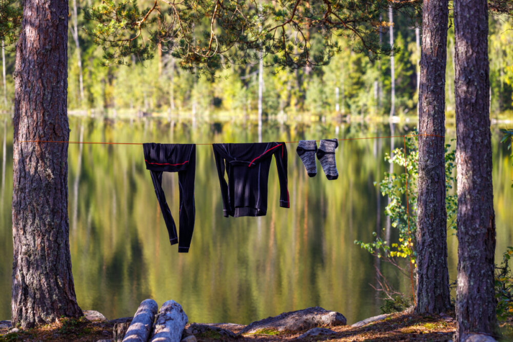 Finding the Perfect Thongs and Underwear for Backpacking 3 Tourist thermal underwear are dried on the shore of a forest lake in the morning. The background is blurred.