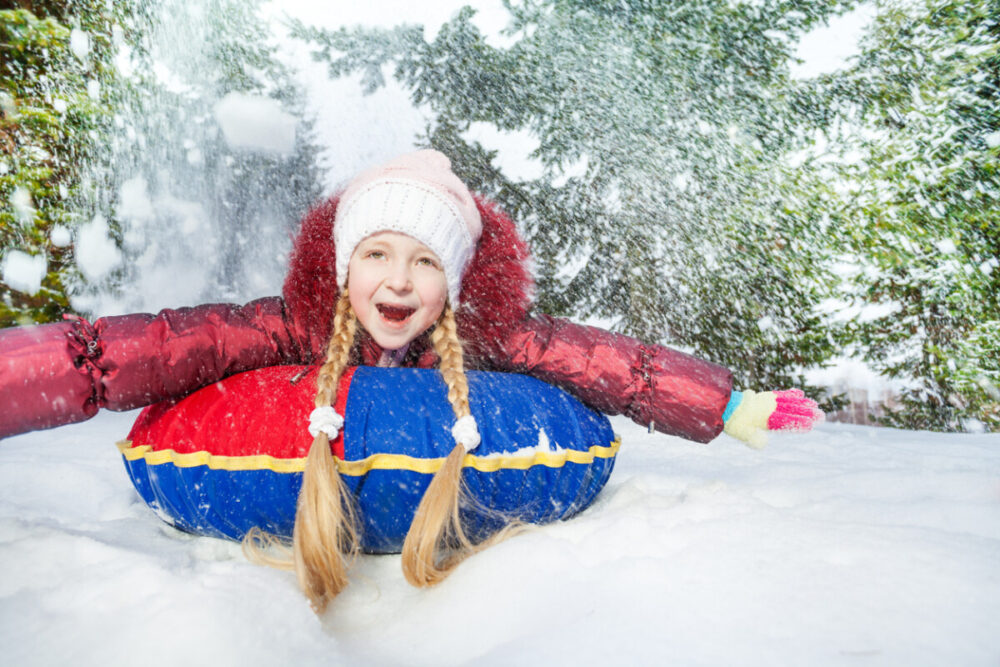How to Keep Children Engaged During a Vacation 3 Excited girl on snow tube in winter during day in the fir tree forest
