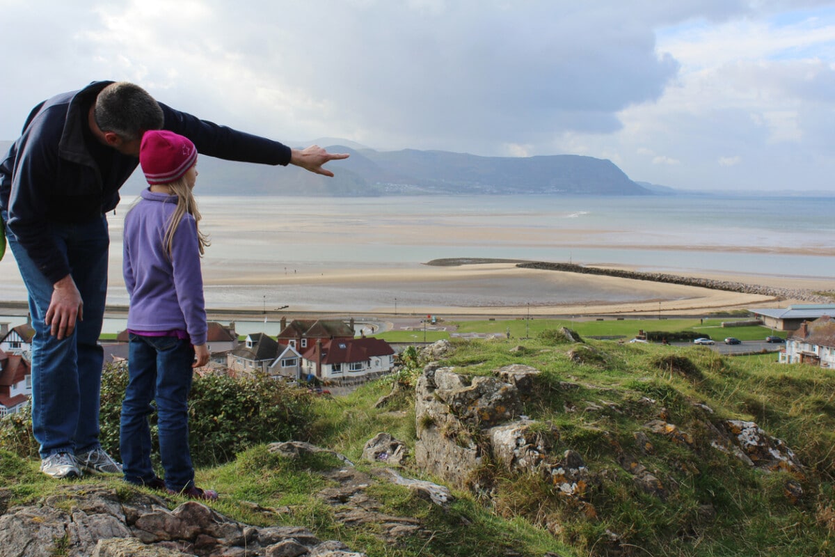 Father is pointing in the distance showing daughter bay of water in Wales