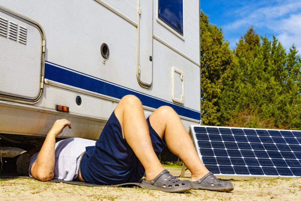 Man lying on ground, repairing bottom of the caravan vehicle.