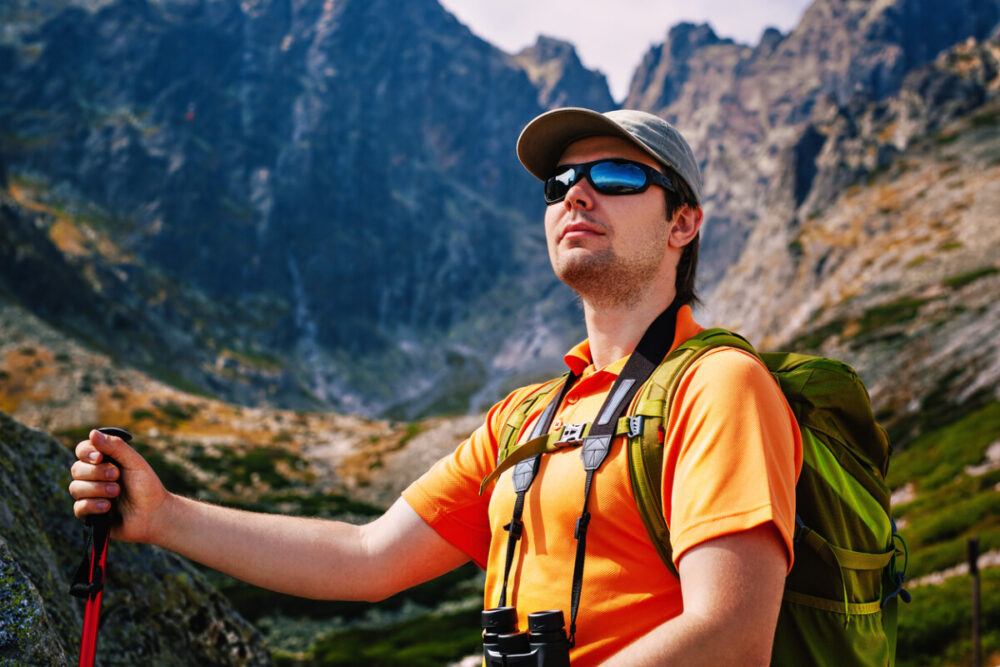 Elevate Your Look: Perfect Eyewear Colors for Every Destination 3 Young man tourist with green backpack and sunglasses portrait on high mountains background
