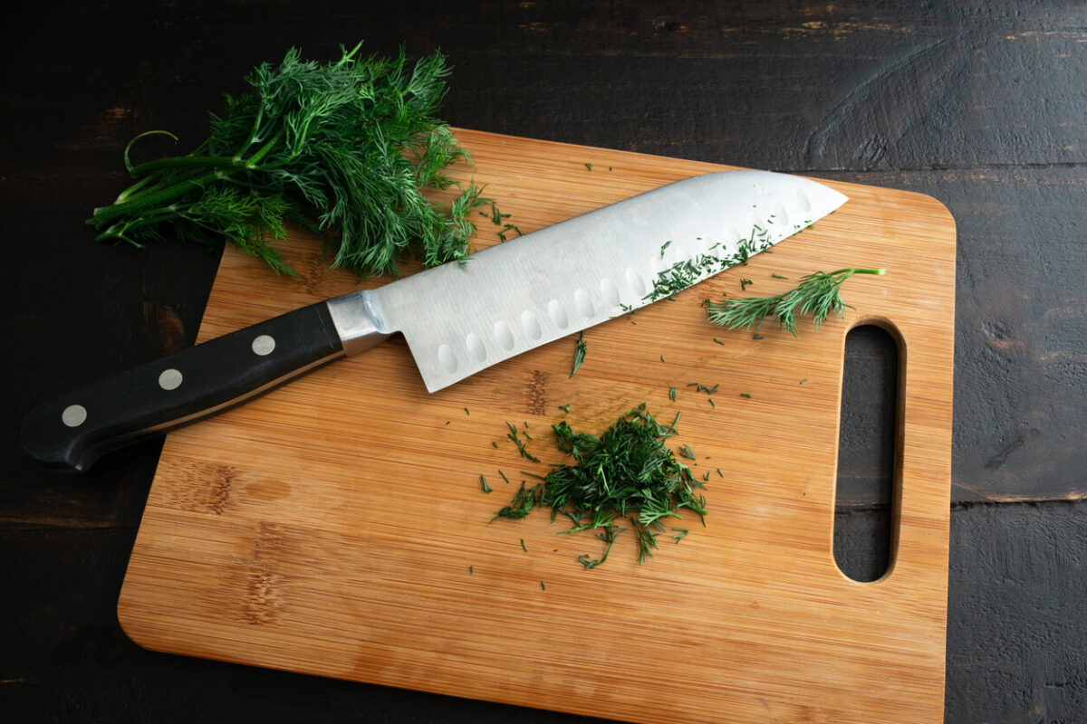 Chef's knife on a cutting board with dill