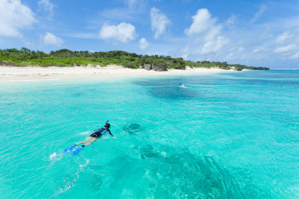 Young woman snorkeling in clear blue water of a coral lagoon around a tropical island, the Yaeyama Islands, Okinawa, Japan
