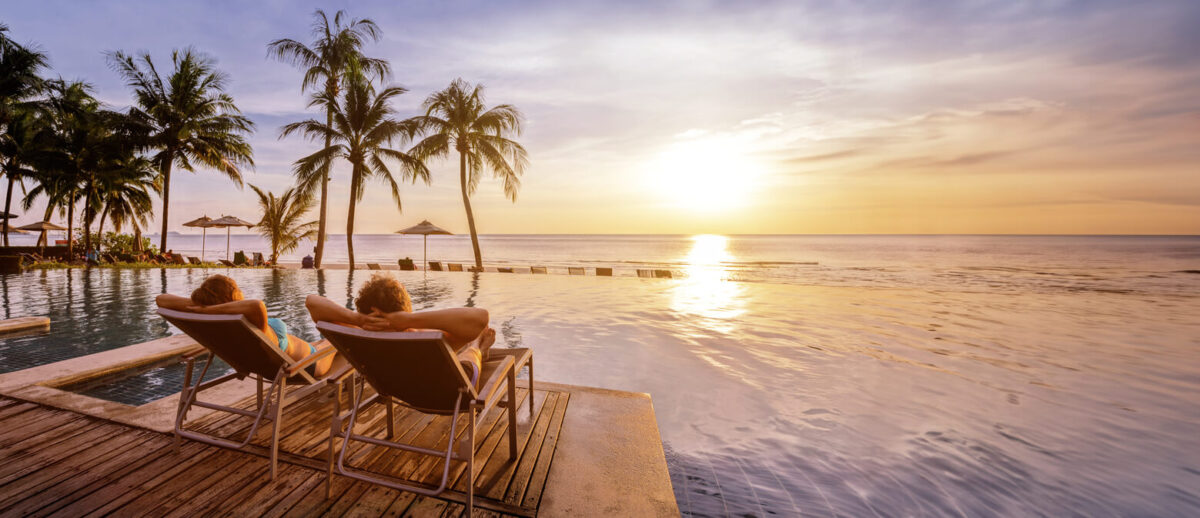 beach holidays for couple in luxury hotel, banner background with copyspace, man and woman relaxing near swimming pool at sunset