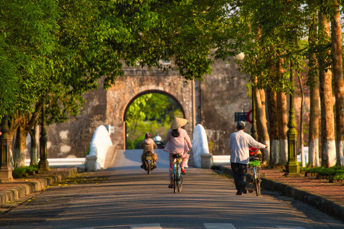 A Hue street scene with traffic heading to an ancient Citadel gate. One of the many things to do in Hue Vietnam