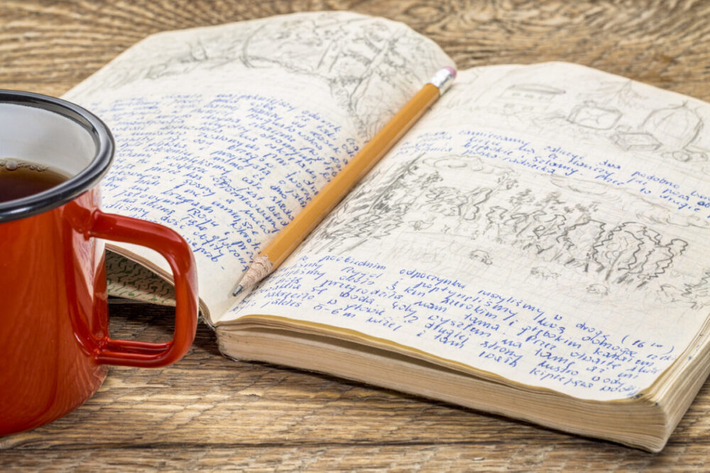 Kayak expedition journal with a cup of tea on a rustic picnic table- handwriting and drawing in pencil. Travel log from paddling trip across north eastern Poland written by me, photographer, in August 1974.