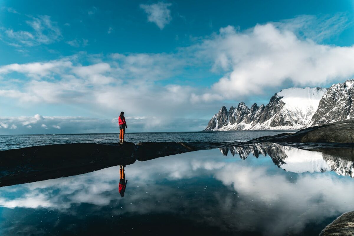 Person standing near a body of water with mountains in background
