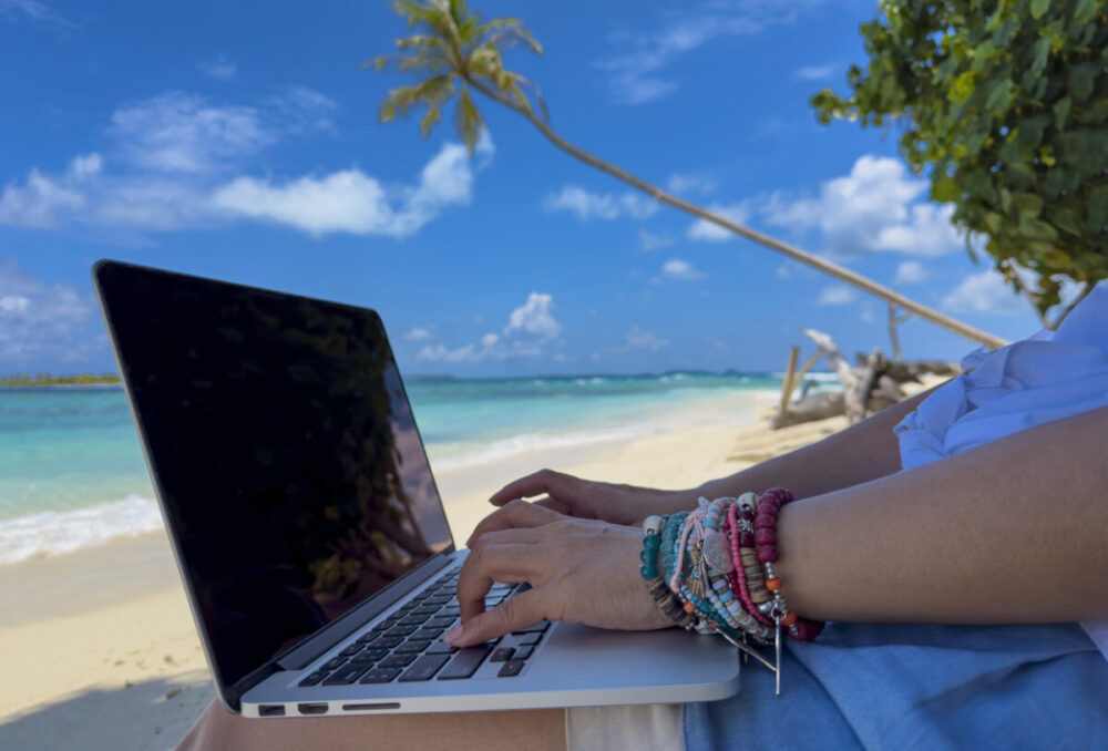 How Citizenship by Investment Can Make International Travel Easier 1 Digital nomad with laptop and running remotely with bright scenic view near poolside on the beach in summer time