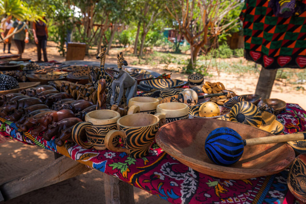Souvenirs Worth Buying During a Multi-Country Journey 3 A colorful assortment of handcrafted African artifacts is beautifully displayed on a wooden market table. The collection includes intricately carved wooden figures, traditional bowls, and vibrant textiles, showcasing the rich cultural heritage and artisanal craftsmanship of the region.