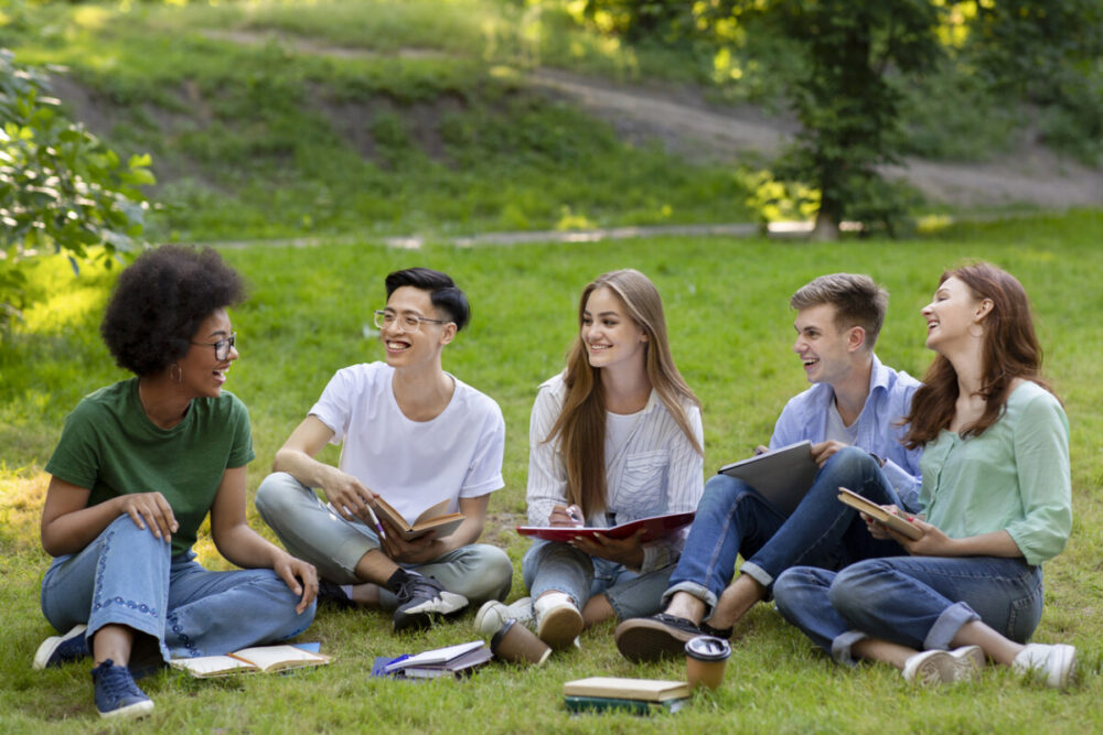 Turning College Visits Into Family Adventures 5 Outdoor portrait of group of college friends resting after classes together, sitting on grass, chatting and laughing, copy space