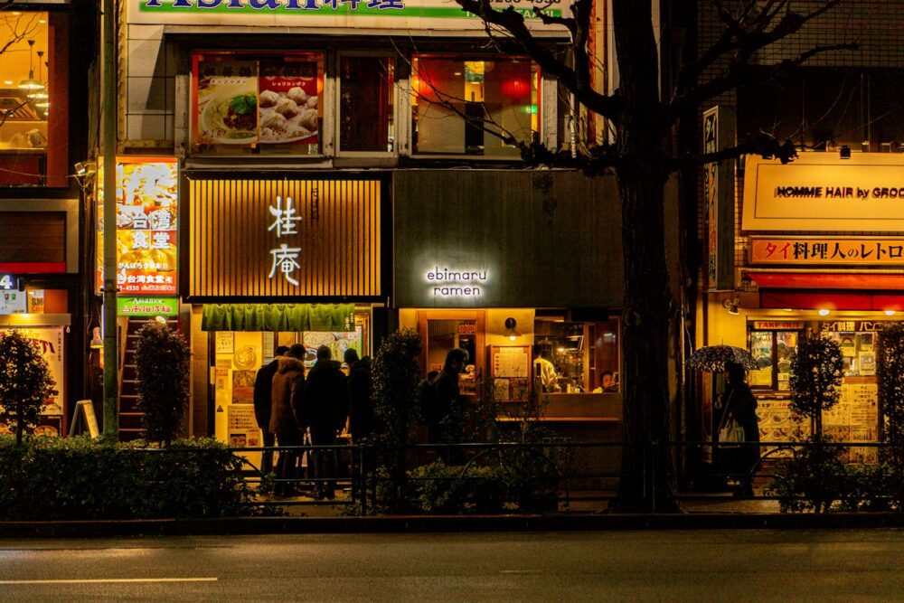 Some of the Best Worldwide Destinations For Food Lovers 3 A bustling street in Tokyo with illuminated ramen shops and patrons at night.