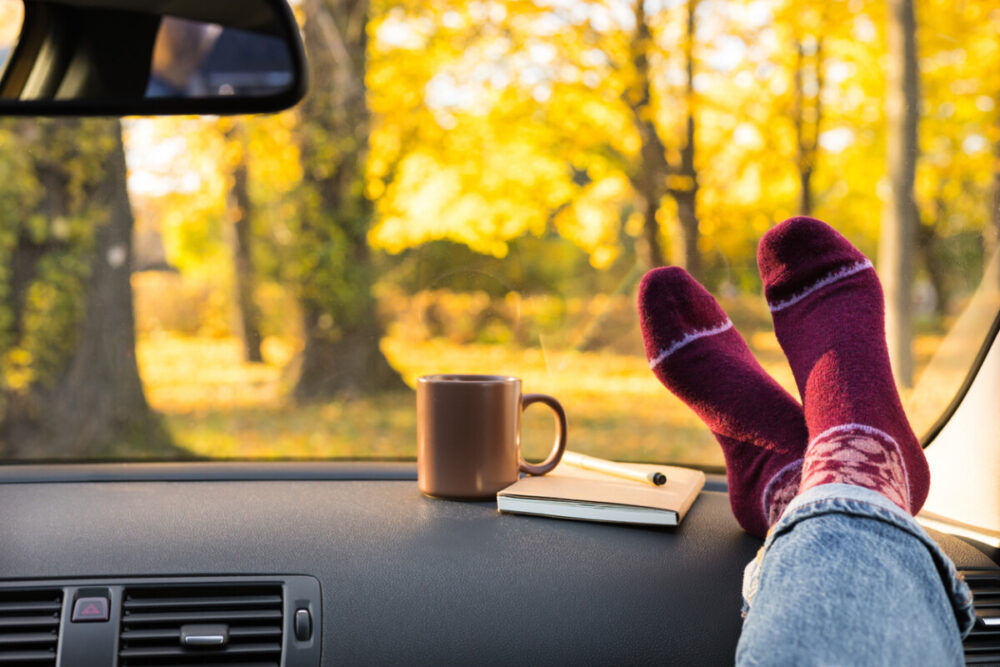 The Rise of Purposeful Travel: What Road Trips Teach Us About Slowing Down 5 Autumn car trip. Woman feet in warm wool socks and cup of tea in the car