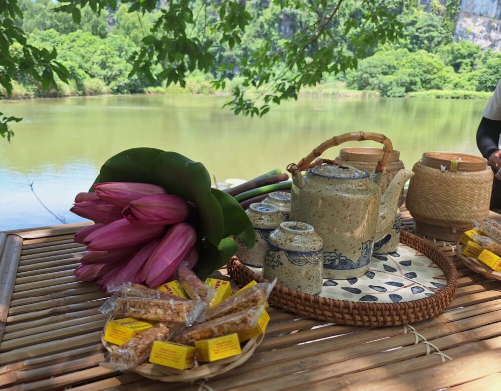 Beyond the Karsts: How Pullman Ninh Binh Unlocks the Real Ninh Binh 1 An image showing a traditional Vietnamese tea setup arranged on a bamboo table overlooking a scenic river and lush green hills