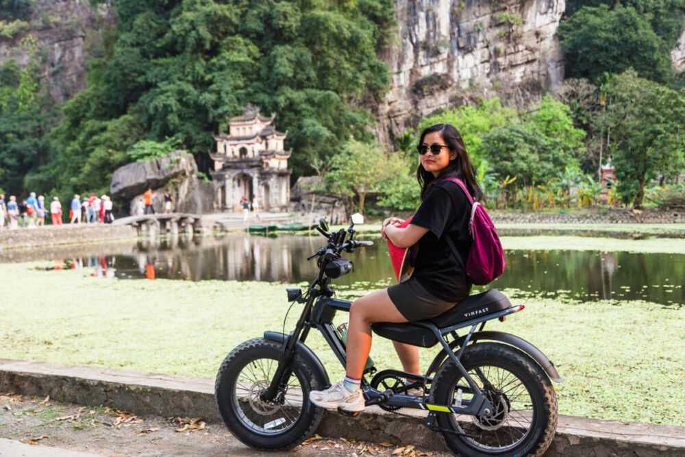 Beyond the Karsts: How Pullman Ninh Binh Unlocks the Real Ninh Binh 4 A young woman with dark hair and sunglasses sits on a black VinFast electric bicycle, looking back over her shoulder.