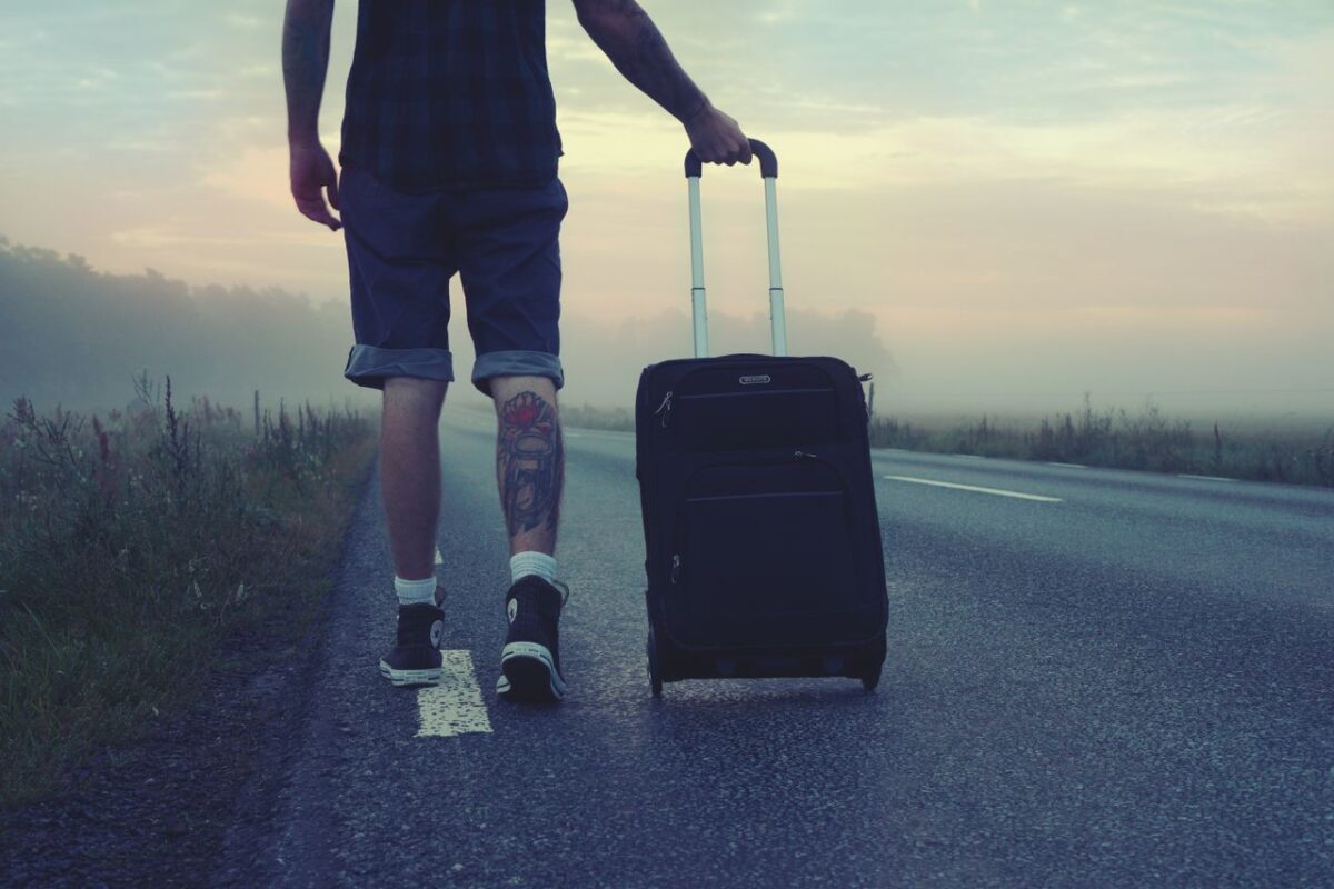 Man walking with a suitcase along a foggy road at sunrise, symbolizing adventure and travel