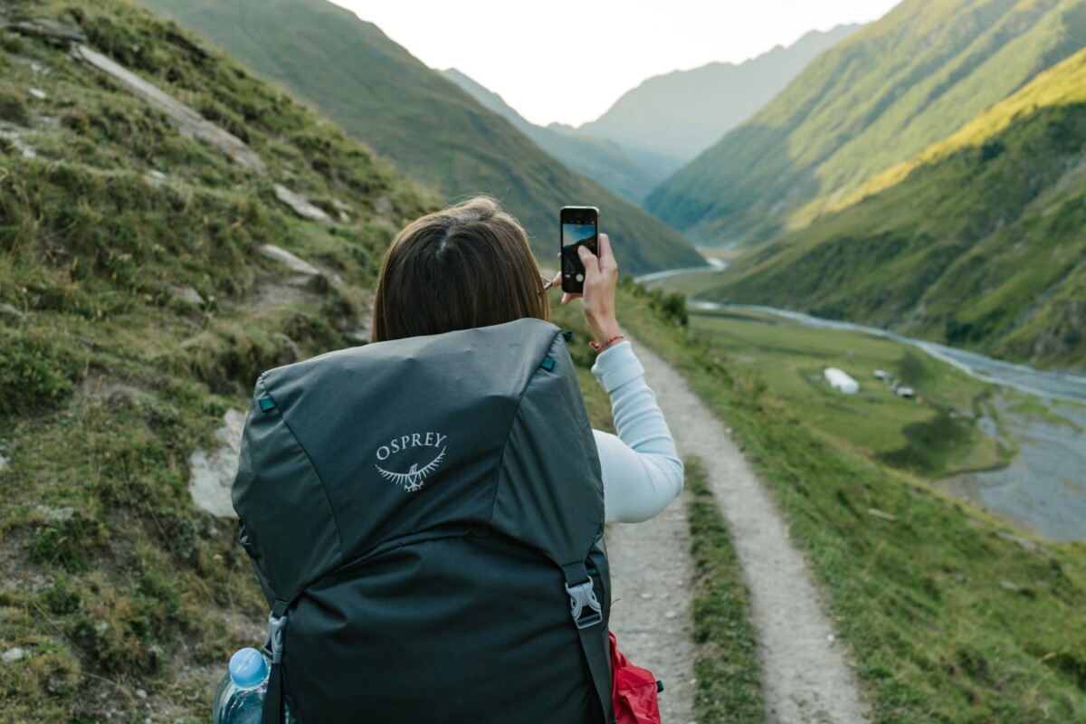 Woman hiking in the Caucasus Mountains with a phone using one of the best travel apps