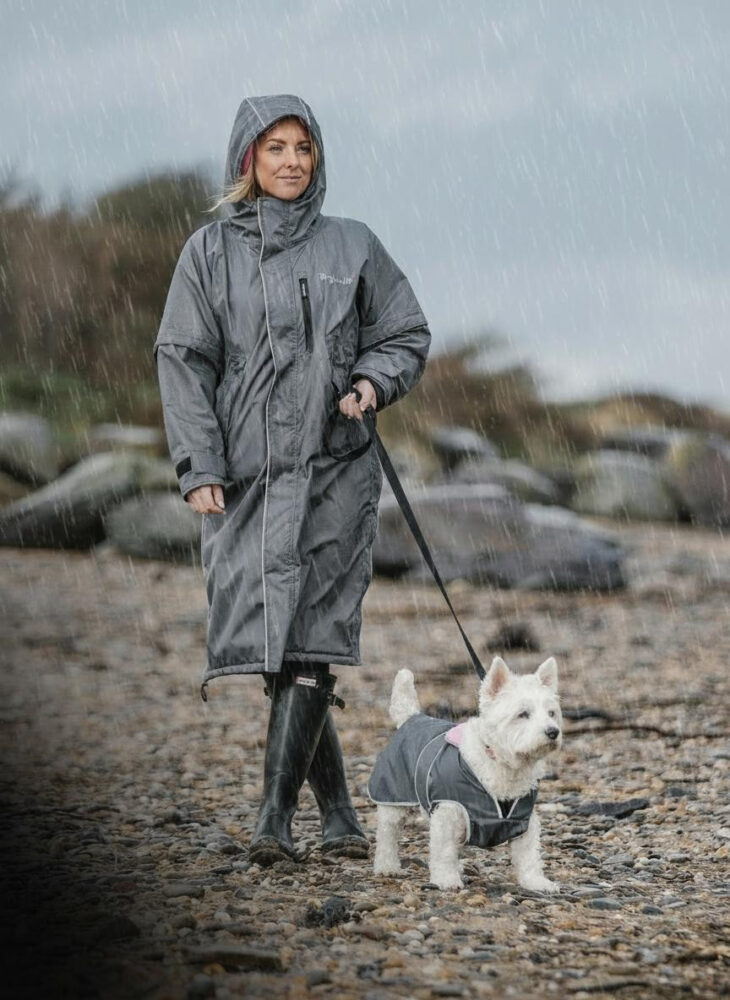 A woman leading a small dog in the rain wearing matching rain coats. 