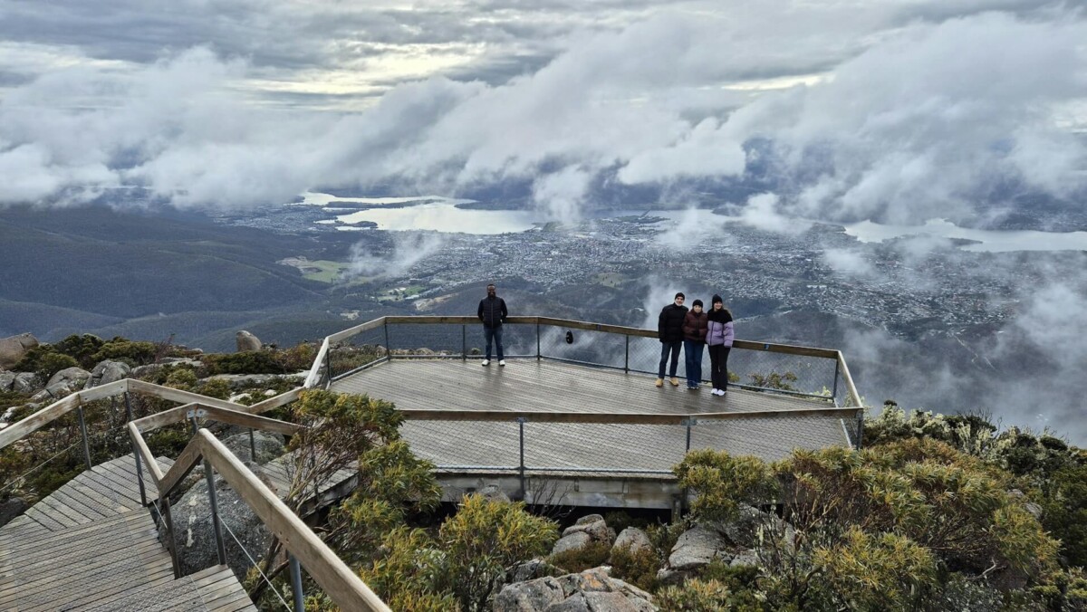 A group of people standing on top of a mountain. Lookout platform on Mt wellington over Hobart Tasmania