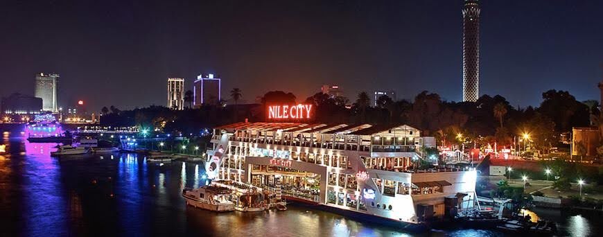 Best Time for a Nile Cruise: A Month-by-Month Guide 3 A lighted party boat at night docked at the edge of the Nile River.