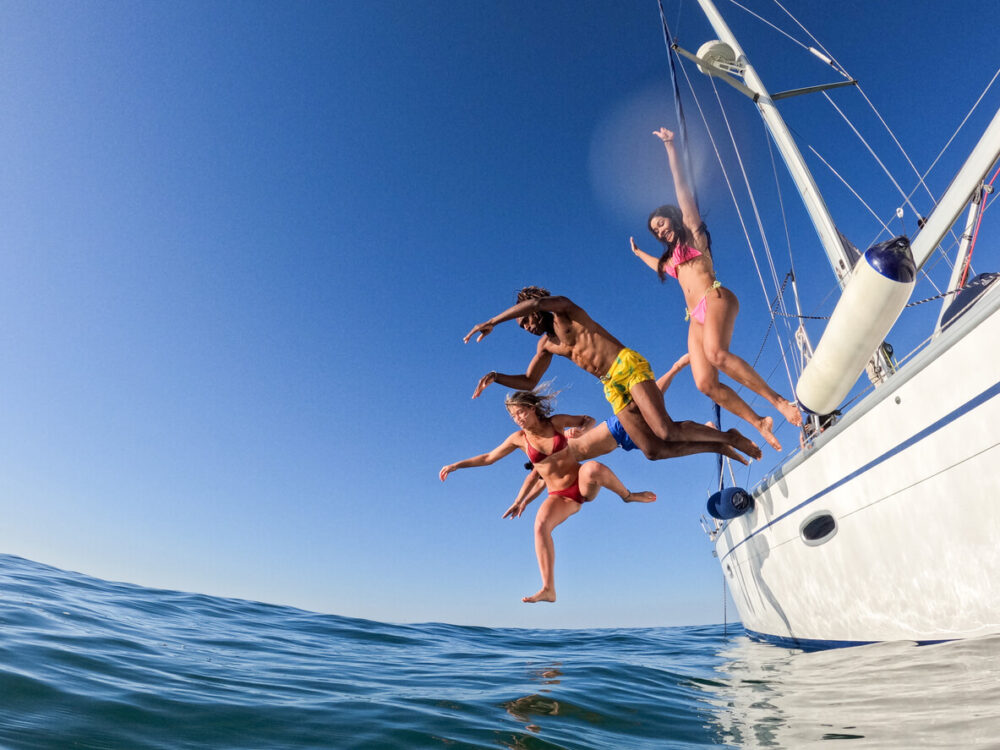 Passengers jumping off the swimming platform of a small cruise ship into the clear blue Adriatic Sea