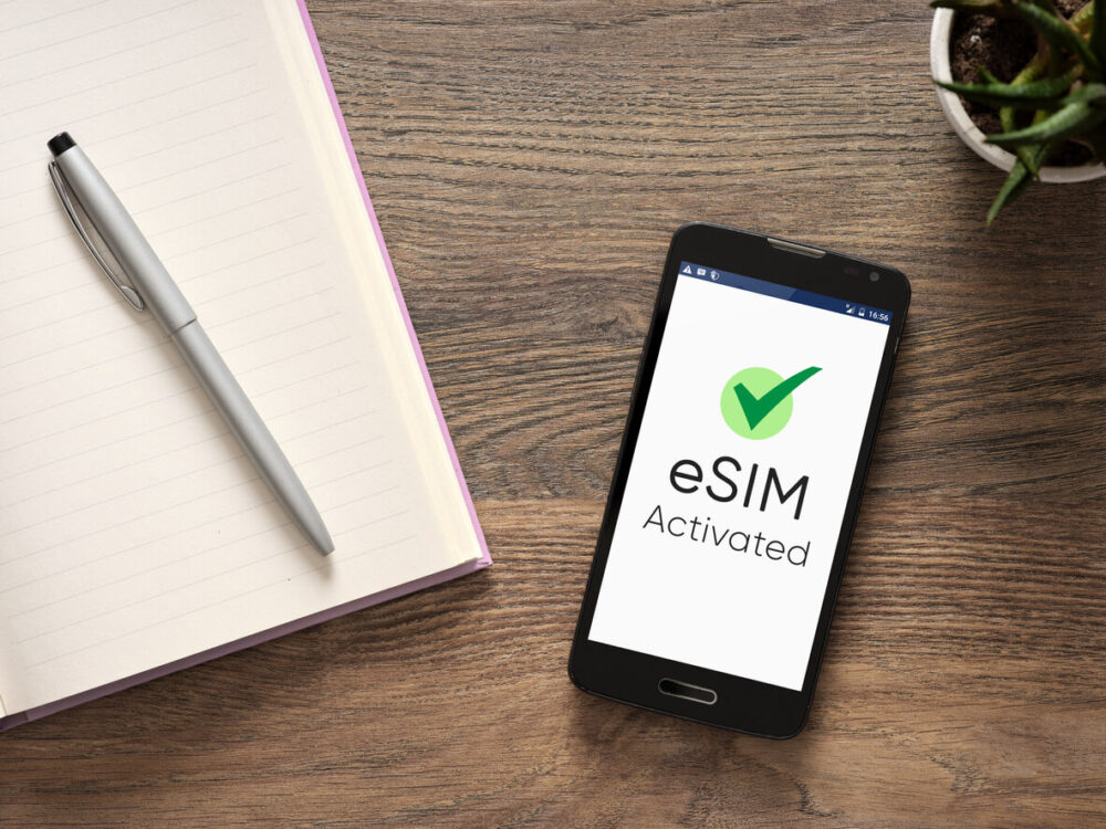 How to Choose the Best eSIM for Europe Travel 4 Smartphone screen showing eSIM activated with a checkmark, resting on a wooden office desk