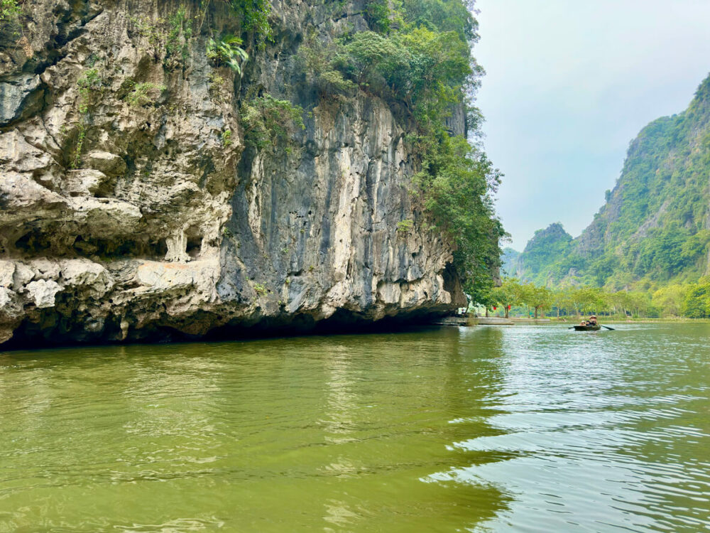 Scene of tourists rowing boats visiting under high limestone cliffs in Tam Coc Ninh Binh province