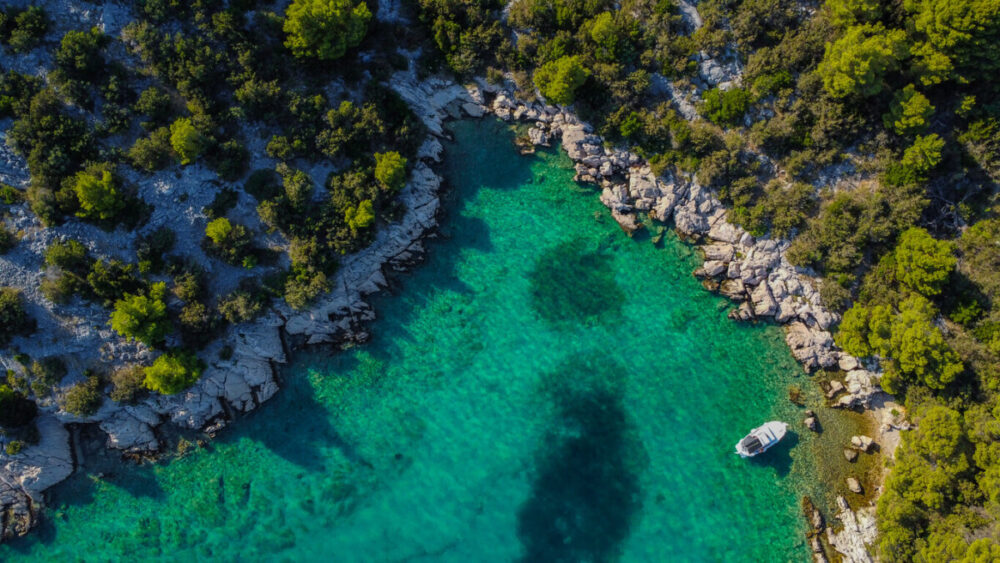 A small cruise ship anchored in a turquoise bay surrounded by pine trees in Croatia