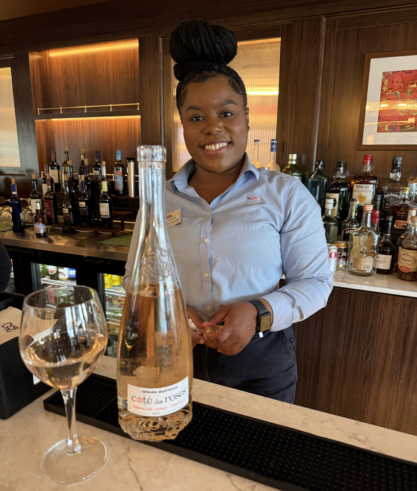 Explore Maine's Coast and Harbors Aboard American Cruise Lines 17 Anaya, Asst. Hotel Mgr., American Maverick, with bottle of rosé wine.