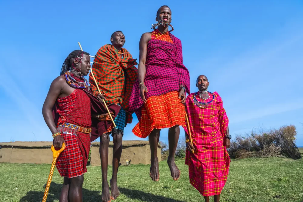 A Guide to an Unforgettable Masai Mara Safari in Kenya 6 Maasai men in colorful traditional clothing performing a jumping dance near Kenya’s Masai Mara National Reserve.