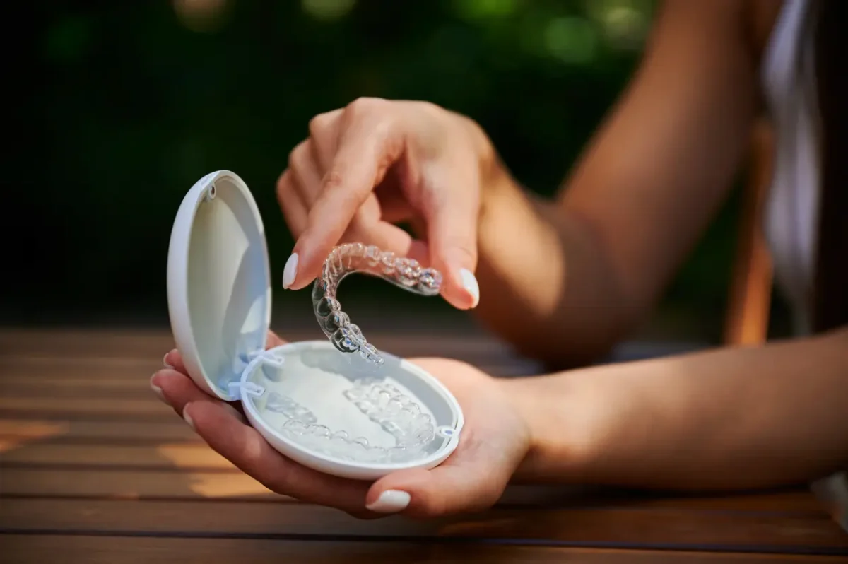 Hand removes transparent dental aligner from open storage case on wooden table