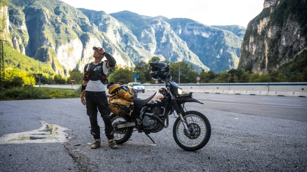 Motorcyclist with loaded bike in mountainous landscape