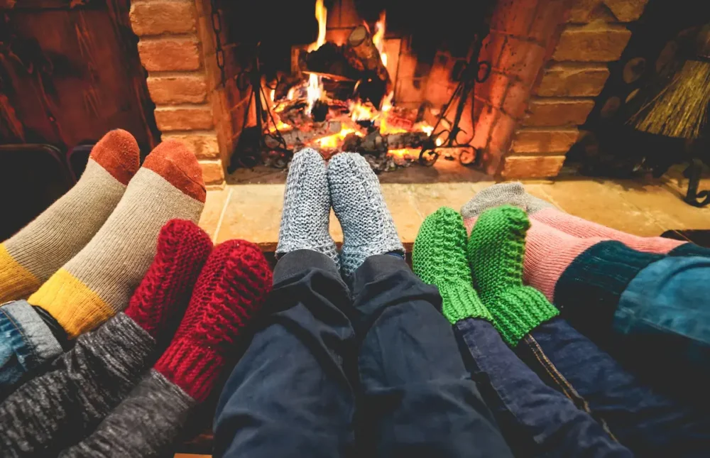 What to Pack for a Cozy Cabin Weekend in Fall and Winter 3 Five sets of stocking feet stretching out to feel the warmth of a fireplace