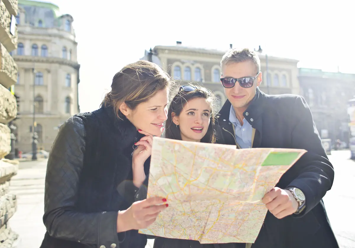 How to Spot Travel Misinformation Online Before You Book 1 Three travelers reading a map under bright sunlight in a European city.